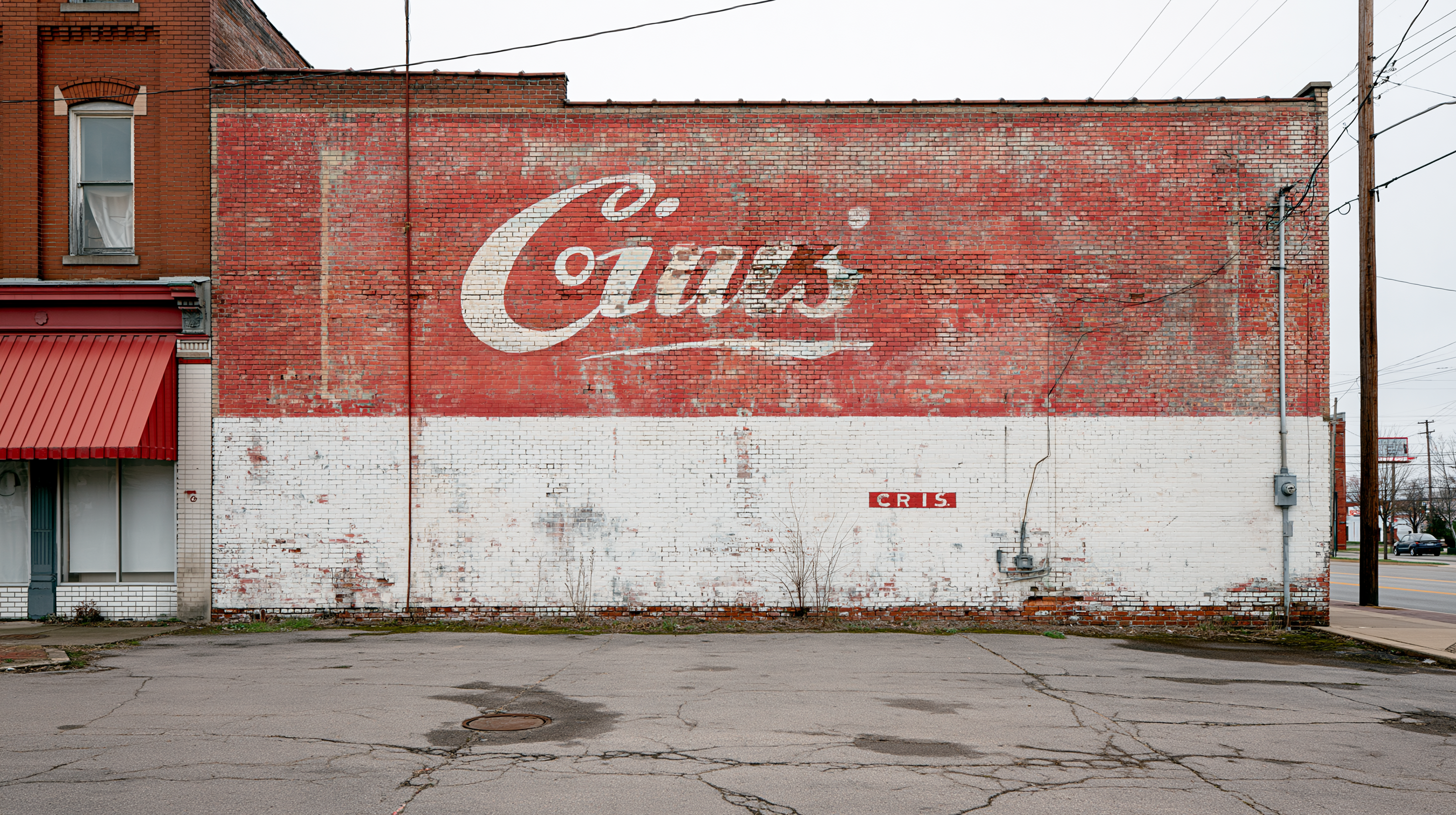 A faded hand-painted shop name half-covered by white paint on a brick wall — the original lettering still legible underneath.