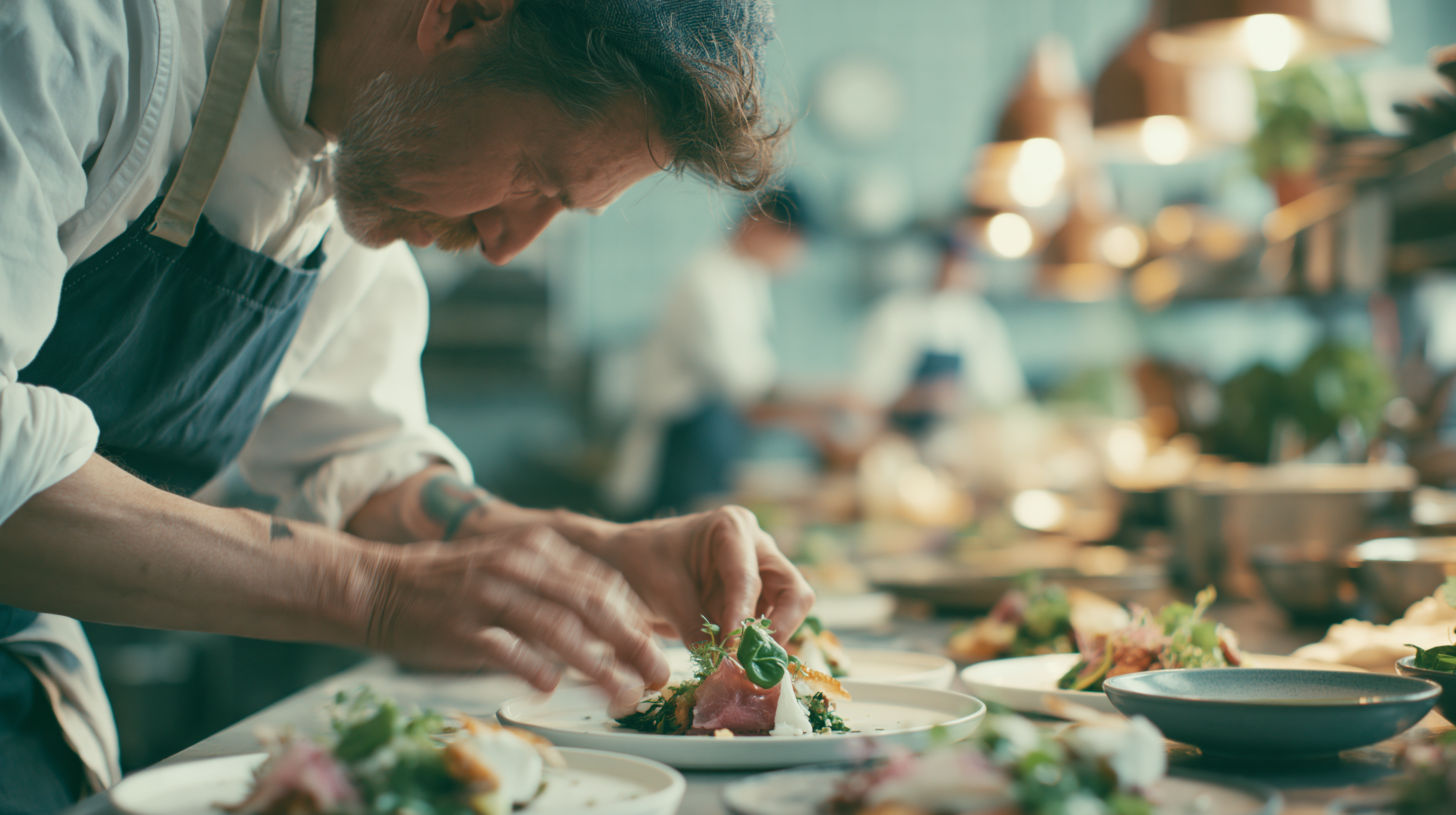 A chef plating a dish at a counter, hands precise on the plate, the kitchen softly out of focus behind.